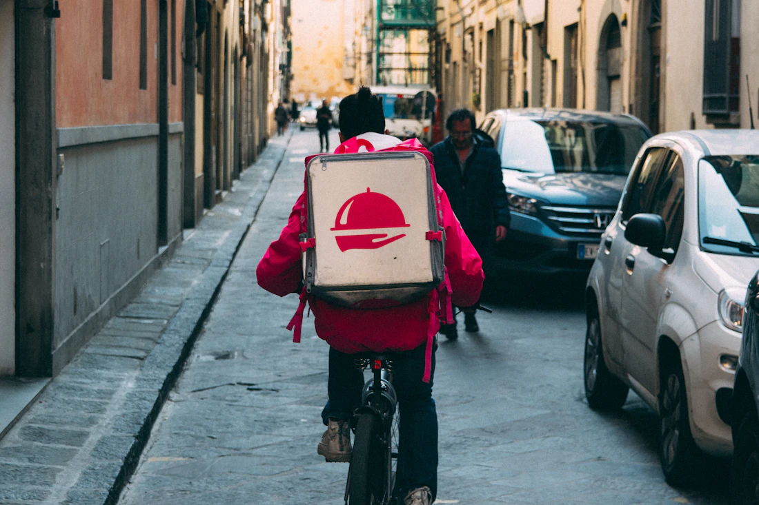 Entregador de bicicleta com mochila de delivery numa rua estreita